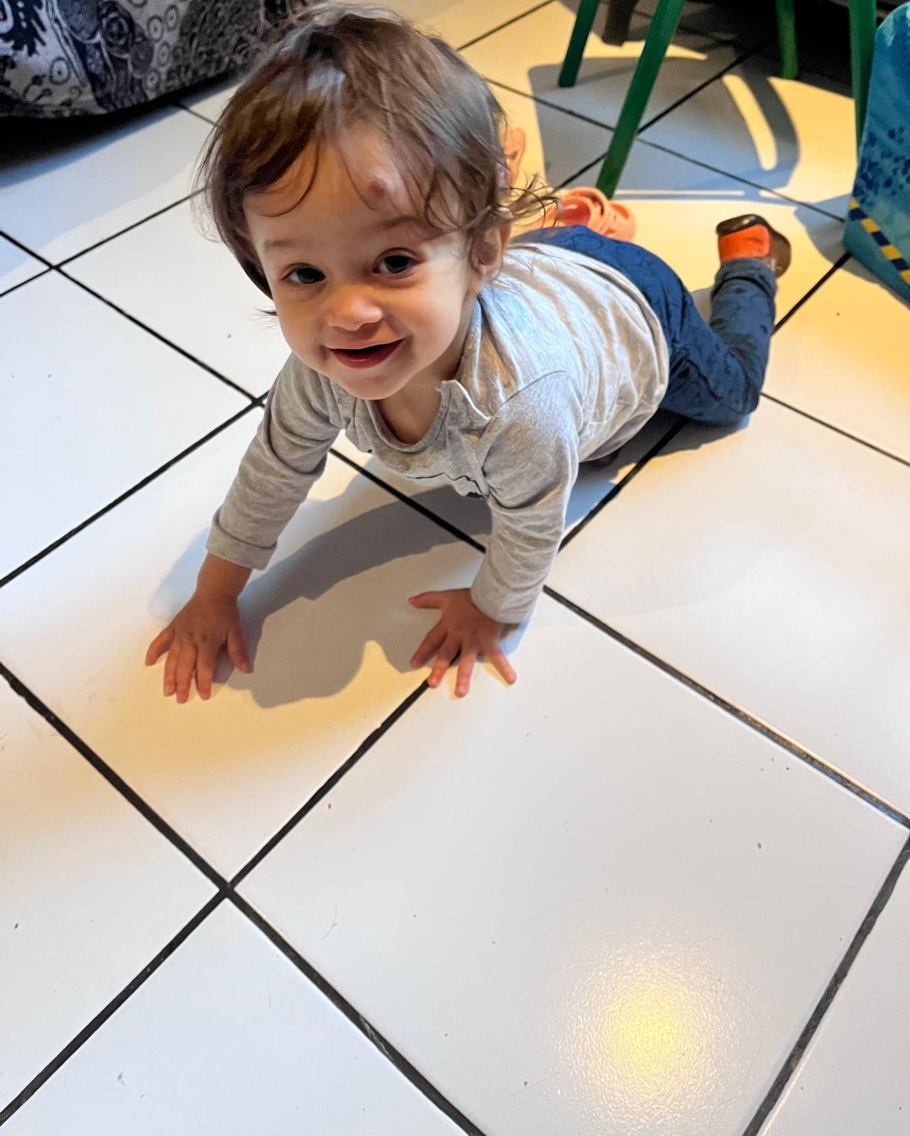 Un tout-petit sourit, à quatre pattes sur le carrelage